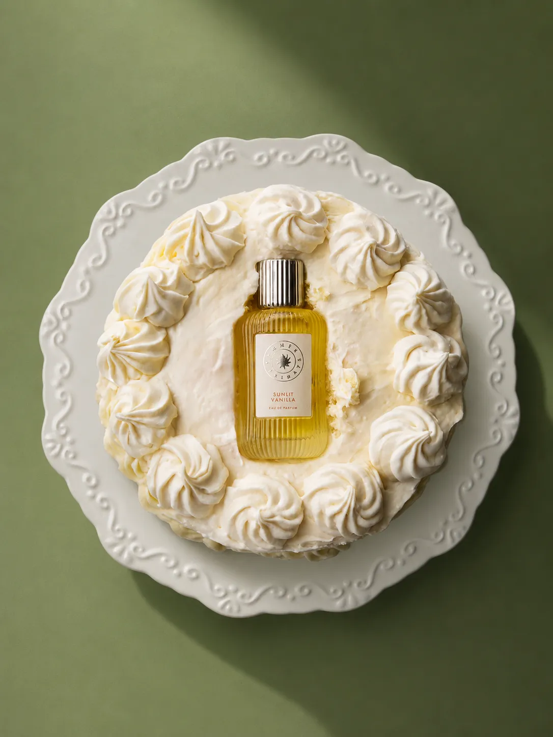 Fragrance bottle set into a whipped cream cake against a green background