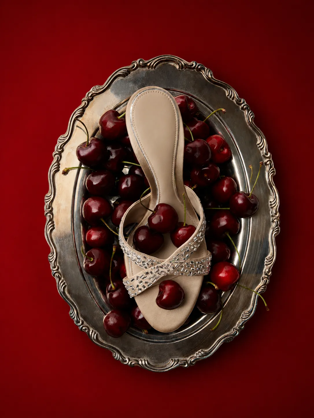 Embellished heeled sandal on a silver tray of cherries against a red background